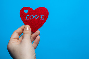 Fototapeta premium Decorative heart of red color with the inscription love in the hands of a man on a blue background