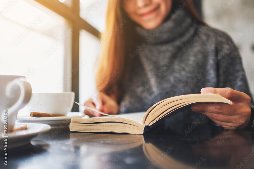 Wall mural closeup image of a beautiful woman holding and reading a book with coffee cup on the table