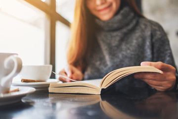 Closeup image of a beautiful woman holding and reading a book with coffee cup on the table