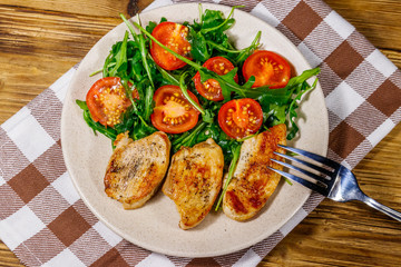 Fried chicken breast with salad of fresh arugula and cherry tomatoes on wooden table. Top view