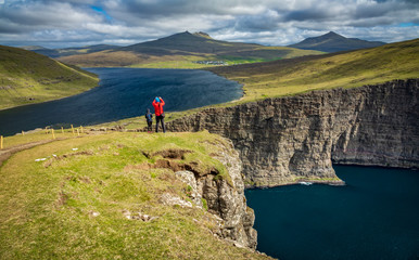 Fototapeta premium Tourists over Sorvagsvatn lake cliffs over the ocean under the clouds, Faroe Islands