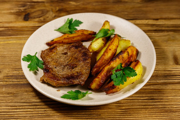Fried beef steak with potato wedges on wooden table