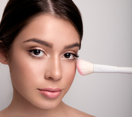 Young beautiful woman holding makeup brush on cheek