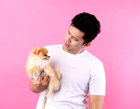 Happy Asian man holding dog pomeranian in hands on a pink background in studio .
