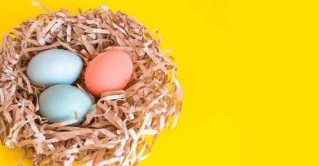 Colored eggs in a nest of paper on a uniform yellow background. Easter holiday card.