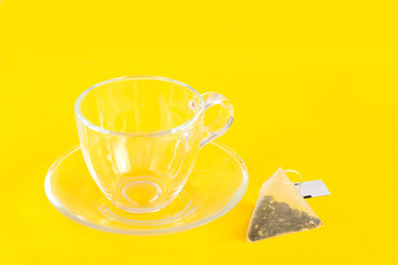Empty cup and saucer made of glass in a uniform yellow background. tea bag