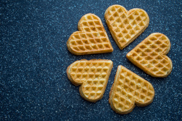 Arrangement of bite-sized heart-shaped waffles on a simple slab background 