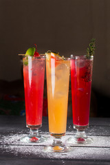 three glasses of fruit red yellow lemonade with ice in highball glasses on black background