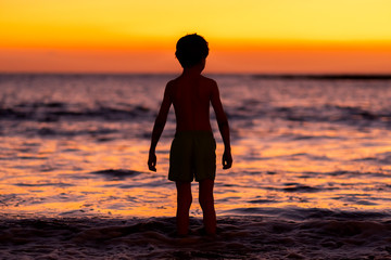 Little boy looking at sunset at the ocean and preparing to swim. © Sk Elena