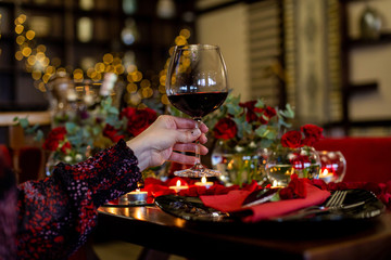 horizontal photo of a female hand that holds a glass with red wine on the background of a beautifully decorated festive table