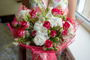 A colorful blossoming flower bouquet of red and white roses and freesia in female hands close up. Beautiful floral background.