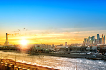 Fototapeta premium scenic skyline of moscow city russia landmark at winter time against beautiful blue yellow orange red sunset sky background. Wide street view of moscow cityscape with frozen river and skyscrapers