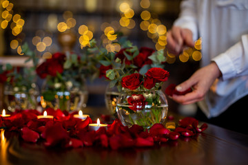 horizontal photo close-up of the process of decorating the festive table with rose petals and candles