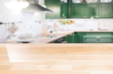 Wooden table top on a blurred background of the kitchen furniture shelves, range hood, and sink. can be used to display or assemble your products