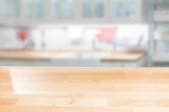 Wooden table top on a blurred background of the kitchen furniture shelves, range hood, and sink. can be used to display or assemble your products
