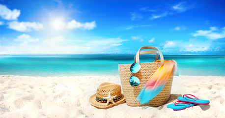 Concept summer holiday. Accessories - bag, straw hat, sunglasses with palm tree reflection, pareo, flip-flops on sandy beach against ocean, blue sky, clouds and bright sun. Beautiful colorful image.