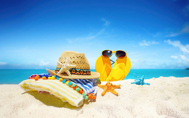 Fototapeta na wymiar Concept summer beach holiday. Beach accessories - straw hat, glasses, towel, starfish, yellow flip-flops on a sandy beach against blue sky with clouds on bright sunny day. Beautiful colorful image.