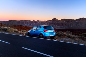 Plakat Tourism car on highway with sunset landscape. Blue car on the background of mountains.