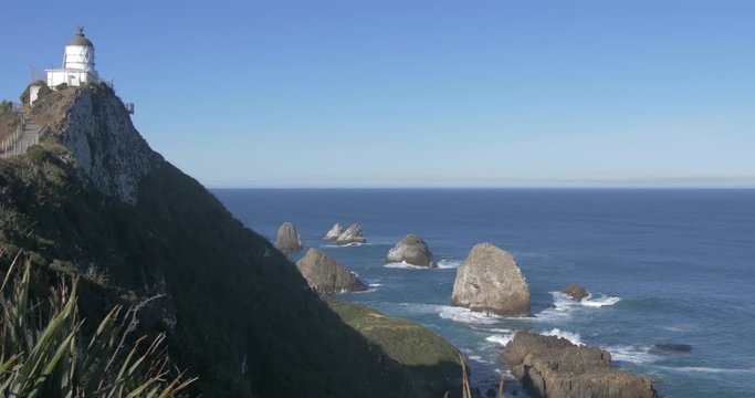 The Nugget Point Lighthouse On Top Of A Steep Rocky Highland With Clumps Of Rocks Beneath Surrounded By Blue Ocean In Catlins, New Zealand - Medium Shot