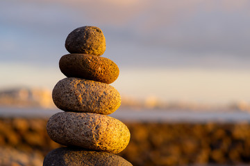 Balanced stone pyramide on shore of the ocean at dawn. Sea pebbles tower closeup symbolizing stability, zen, harmony, balance.