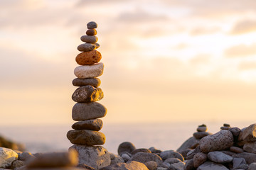 Balanced stone pyramide on shore of the ocean at dawn. Sea pebbles tower closeup symbolizing stability, zen, harmony, balance.