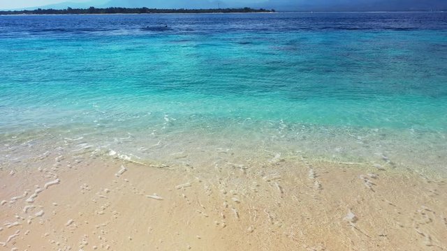 foamy waves washing the sandy shore, tropical beach background. Revealing mountains and a small island in the background