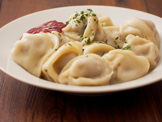 Portion of Russian classic big size dumplings on a white plate with tomato ketchup and herbs. Dark wood table surface.