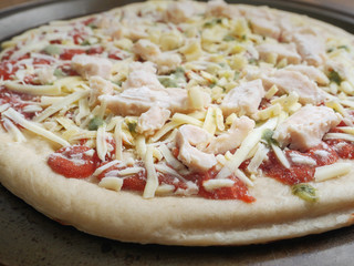 Uncooked raw pizza with chicken fillets cheese on a metal trey and wooden table, Ready to go in the oven. Close up.