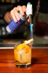 The bartender burns a cinnamon stick with a gas burner in the bar.
