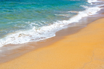 Fototapeta na wymiar Waves on a beach with orange sand and blue water