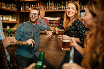 Group of friends drinking beer, chatting and having good time at pub. Night out.