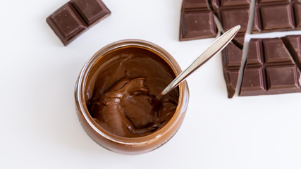 Chocolate mousse  in a jar. There is spoon in it. There are few pieces of dark chocolate near it. Isolated. White background. 