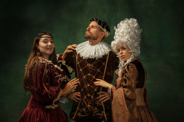 Love games pay attention. Portrait of medieval young people in vintage clothing on dark background. Models as a duke and duchess, princess, royal persons. Concept of comparison of eras, modern