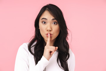 Image of young brunette asian woman holding finger on lips