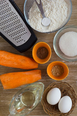 Grater, carrot, eggs, oil, sugar, flour, spices as ingredients for carrot pie on the wooden background