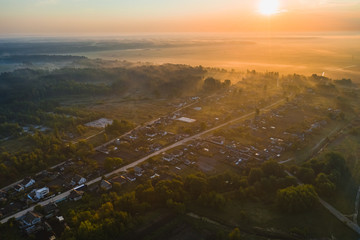 Morning landscape with a village and fog near the forest and fields. Aerial view