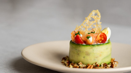 Cucumber, salmon and soft cheese salad with small eggs, cherry tomatoes ant some nuts. Parmesan cheese crisp. Restaurant plating.