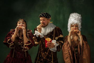Taste of future. Portrait of medieval young people in vintage clothing on dark background. Models...