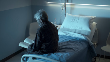 Lonely elderly man reading a book at the hospital