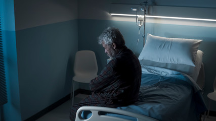 Depressed lonely senior sitting on a hospital bed at night