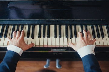 A male musician plays the piano, presses hands and fingers on black and white keys close-up....