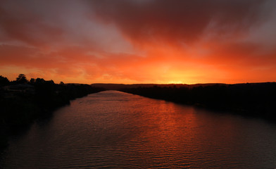 Fototapeta premium Red sky sunset over river with distant mountains