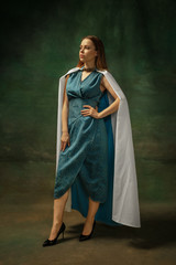 Elegance posing. Portrait of medieval young woman in blue vintage clothing on dark background. Female model as a duchess, royal person. Concept of comparison of eras, modern, fashion, beauty.