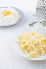Grated cheese, on a background of grater and flour in a plate with broken poison on top. The concept of cooking pizza, baking with cheese.