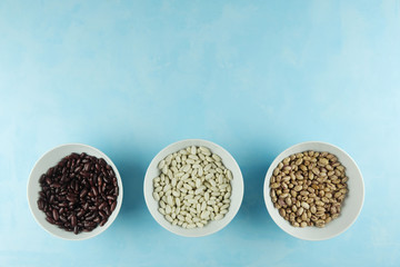 Three types, varieties of kidney beans are in white ceramic biscuits, cups on a blue table. Colorful beans. Place for text. Bean source of protein
