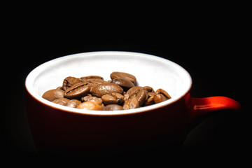 Coffee beans in a red cup on a dark background. Photo in the dark