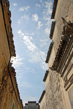 Xidi Ancient Town in Anhui Province, China. Roofs and white walls in the old town of Xidi set against a blue sky with clouds. Tiles and eaves of old roofs in the historical town of Xidi in China. 