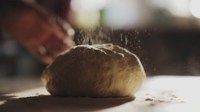 Female cook hands kneading dough in flour on the table, slow motion, sunlight from the window illuminates the scene.