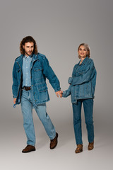 stylish man and smiling woman in denim jackets holding hands on grey background