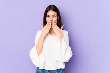 Young caucasian woman isolated on purple background shocked covering mouth with hands.